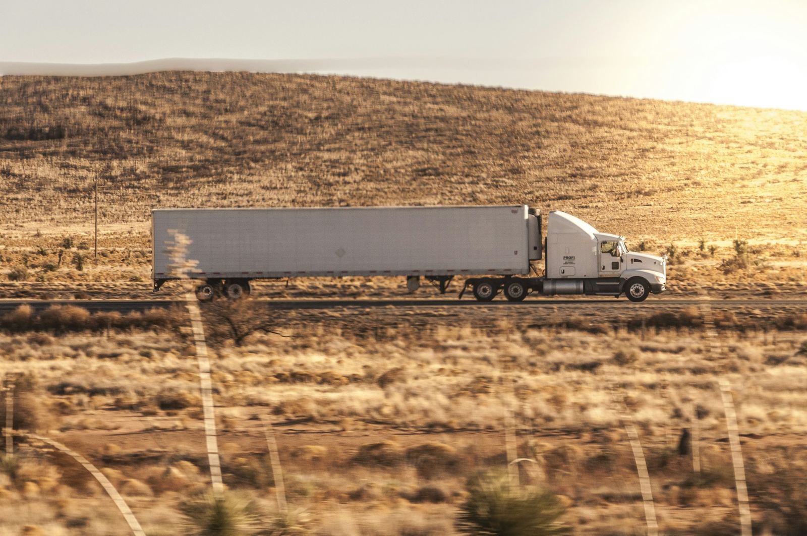 A white semi truck on a highway through golden hills