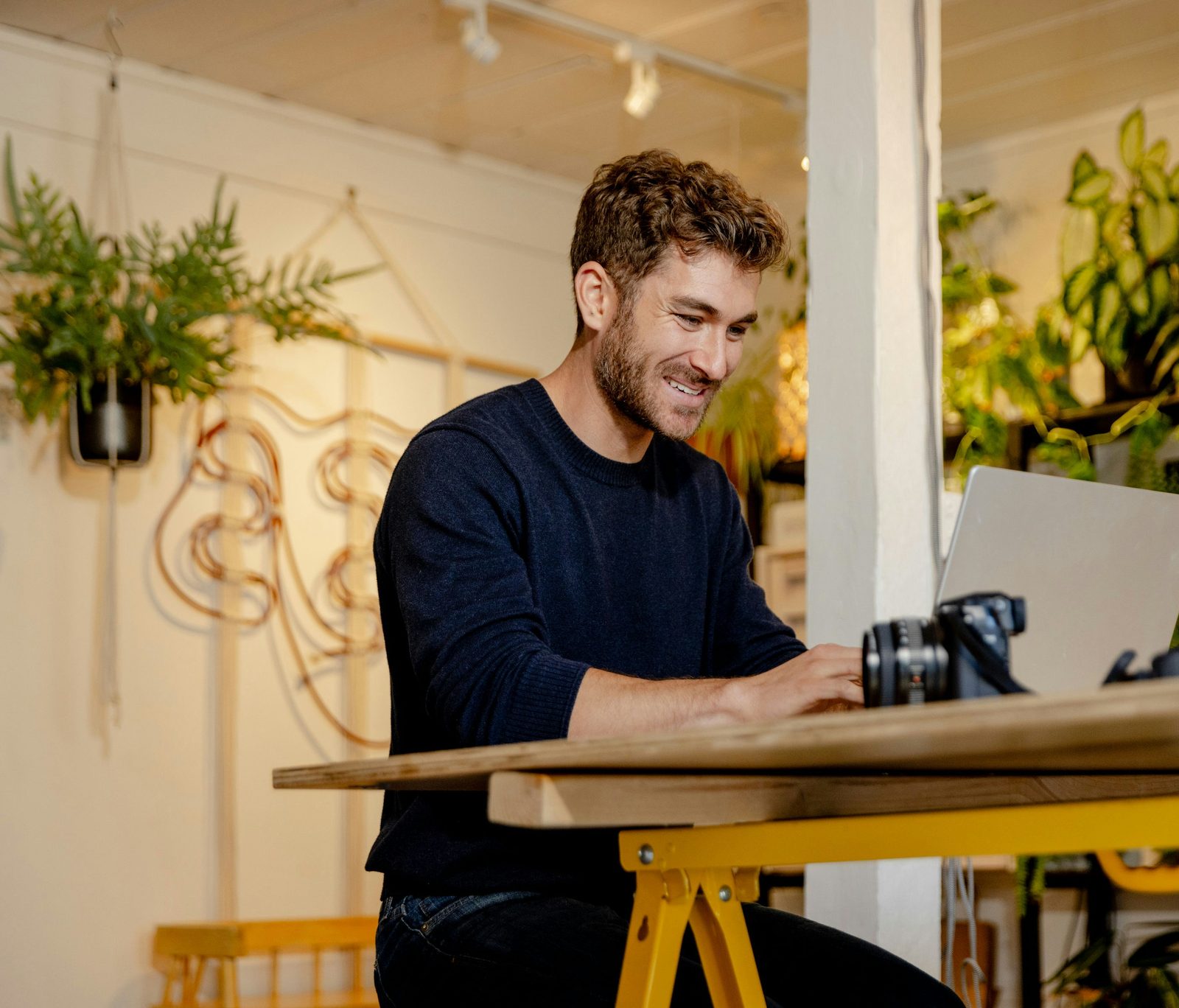 A business owner working on a laptop in his plant-filled shop