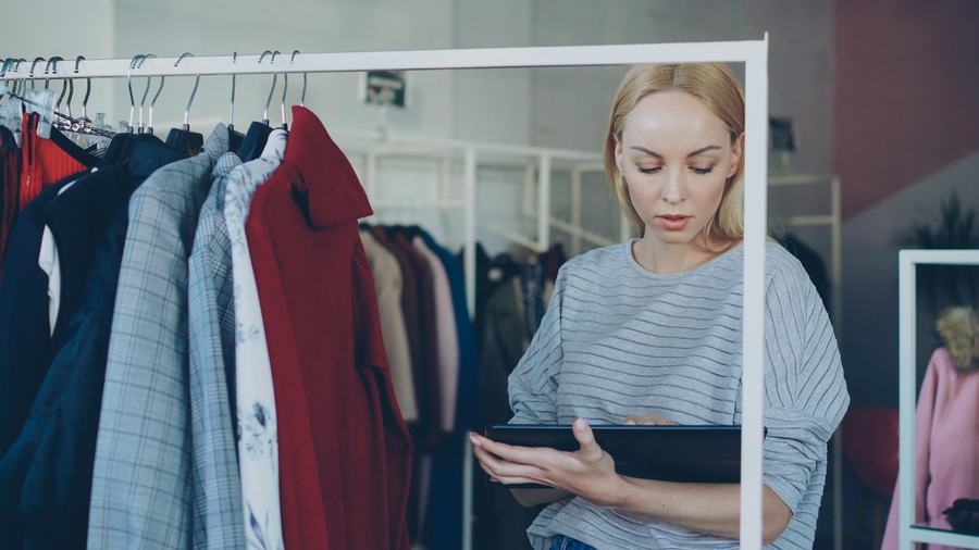 A shop owner checking stock on a tablet in her clothing store