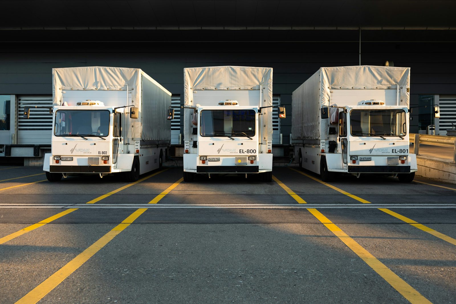 Three white box trucks parked side by side at a loading dock