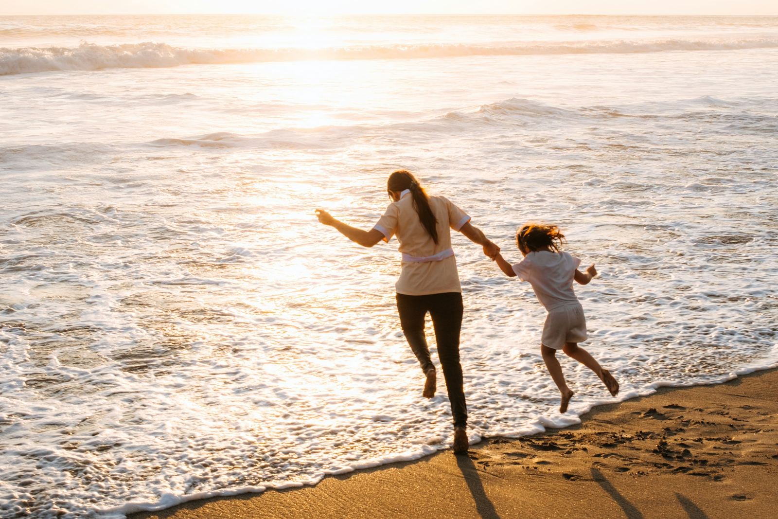 A mother and child running on the beach at sunset
