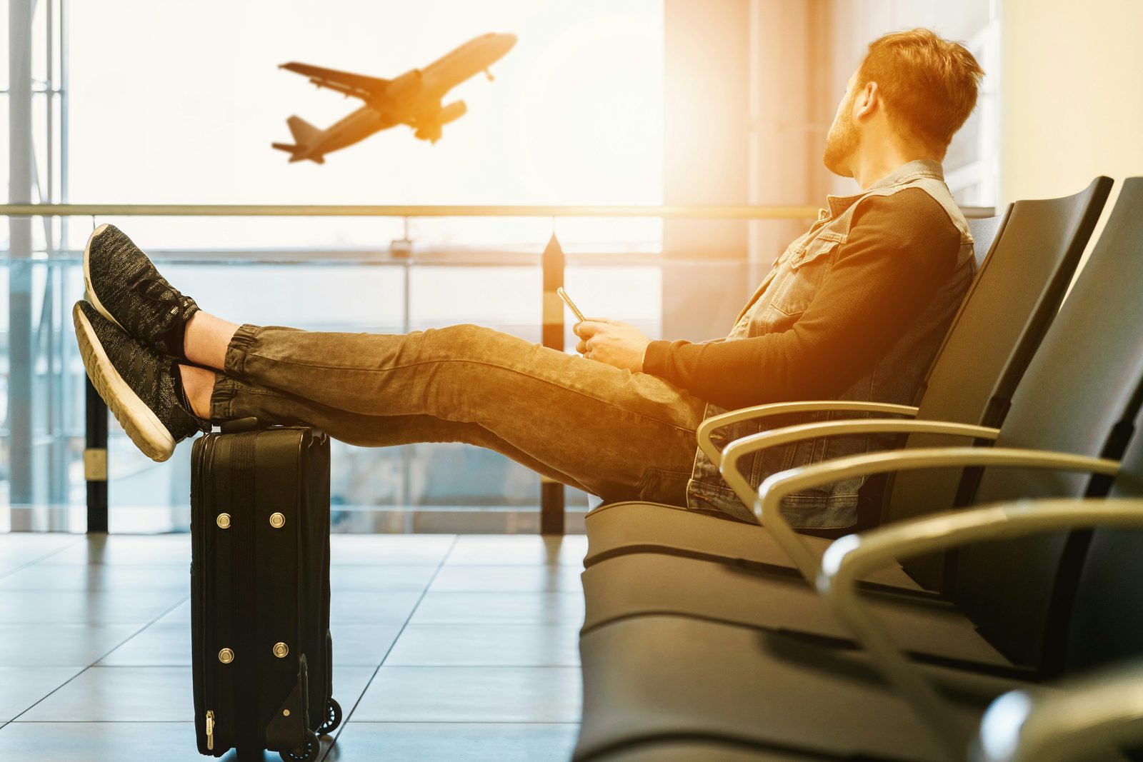 A traveler resting his feet on his suitcase at the airport as a plane takes off
