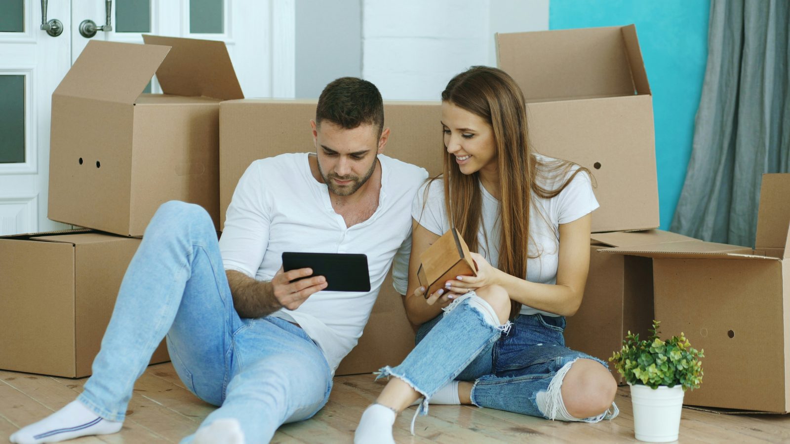 A couple sitting among moving boxes, looking at a tablet