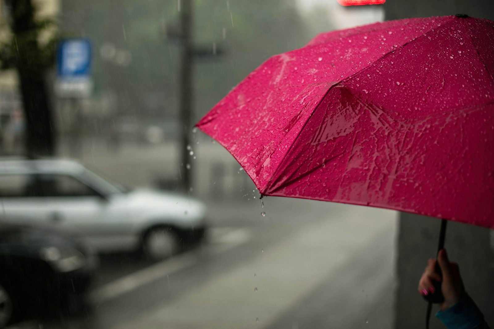 A pink umbrella held up in the rain on a city street