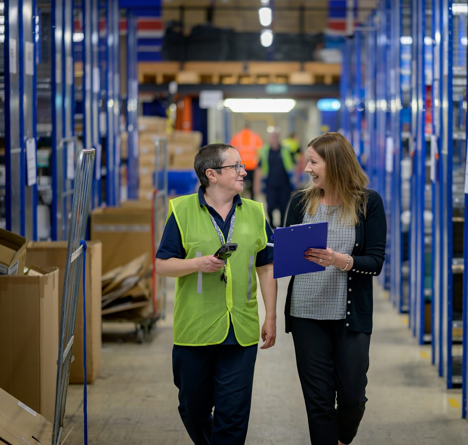 Two warehouse employees talking in an aisle, one in a hi-vis vest